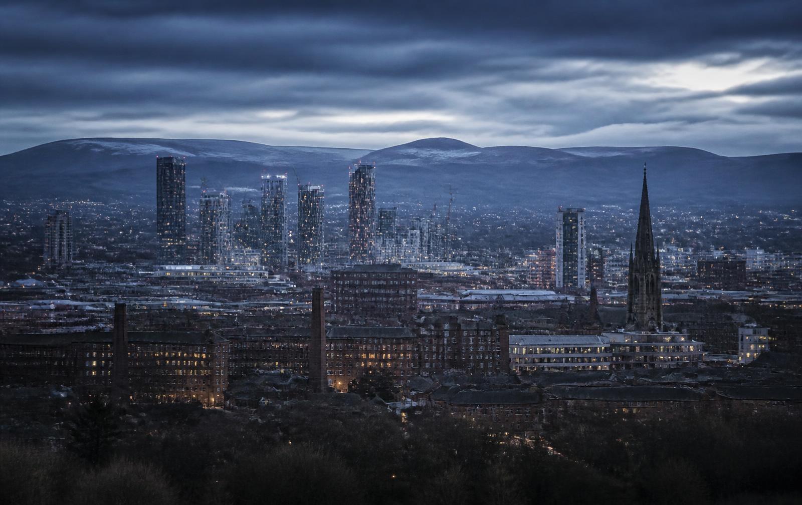 North West of England at dusk — Manchester skyline against the Pennine hills under a moody overcast sky
